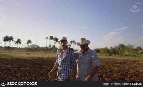 Farming and cultivations in Latin America. Hispanic farmer walking with his son in a cultivated field at sunset. The man embraces the teenager and plans the job to be done. Steadicam shot