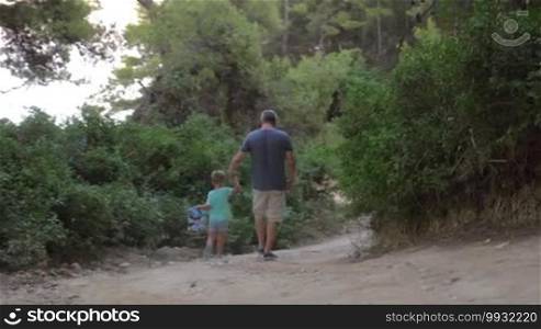 Father and son walking away in forest. Unrecognizable