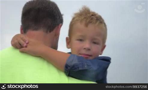Father walks and keeps in arms his little son. Family walk on the street. Son's face close-up