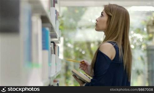 Female blonde college student taking book from shelf in library. Rack focus