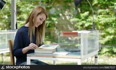 Female college student choosing book on shelf and sitting in library. Dolly shot