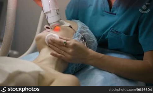 Female cosmetician providing a laser facial treatment for a woman in clinic.