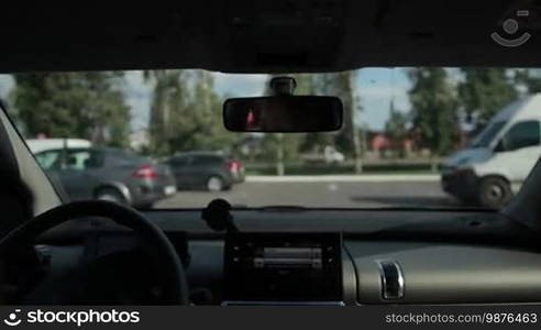 Female driver looking for empty space in open parking area near shopping mall on sunny summer day. View from inside of auto. Woman parking her car into the parking lot.