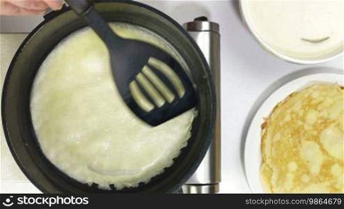 Female hands baking pancake into a frying pan