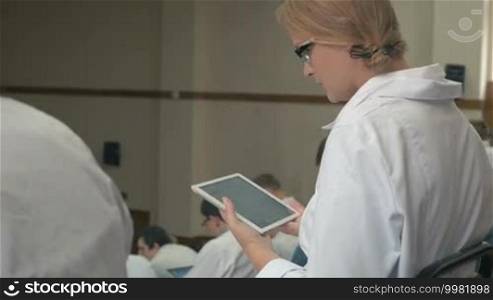 Female medical student or doctor typing on digital tablet in auditorium during lecture or conference