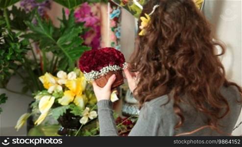 Florist arranging rose heart-shaped bouquet is surrounded by gypsophila in flower shop. Focus on the bouquet