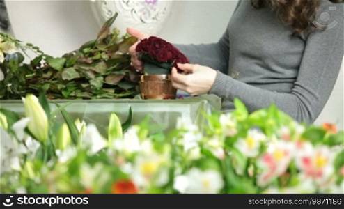Florist creating red roses bouquet arranged in heart shape in flower shop
