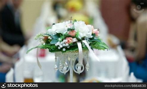 Flower arrangement on the wedding dinner table with guests in the background