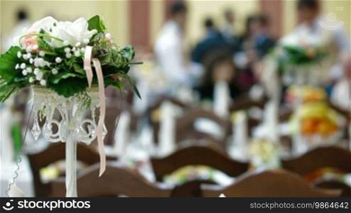 Flower arrangement on the wedding dinner table, with guests in the background