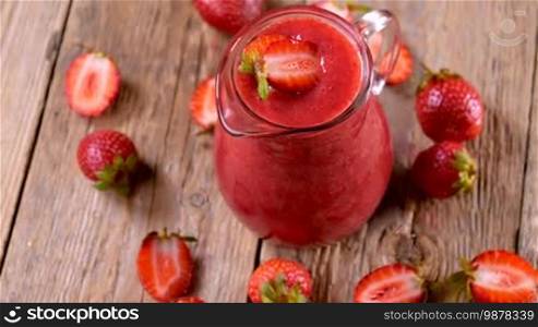 Fresh strawberry smoothie spinning on wooden table ready to drink. Healthy drinking concept.