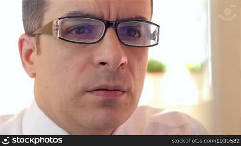 Frustrated and angry businessman with glasses sitting in front of computer monitor.
