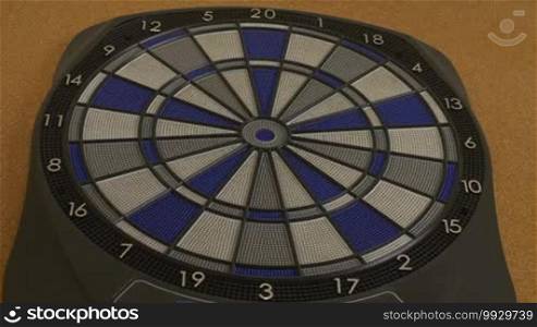 Full shot of electronic dartboard with dart finally hitting bullseye at the third and last one