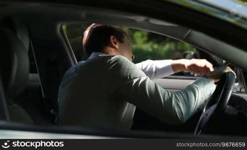 Furious businessman driving car at traffic jam and arguing. Side view. Frustrated man in formal wear got stuck in traffic jam on the road while driving auto to work on sunny summer day.