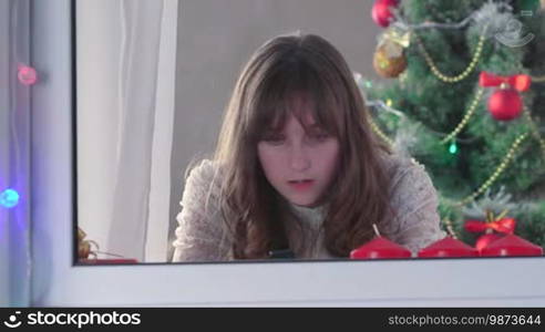 Girl using smartphone near Christmas tree, typing something