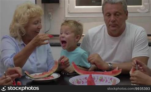 Grandmother feeding a little grandchild with watermelon in a playful manner