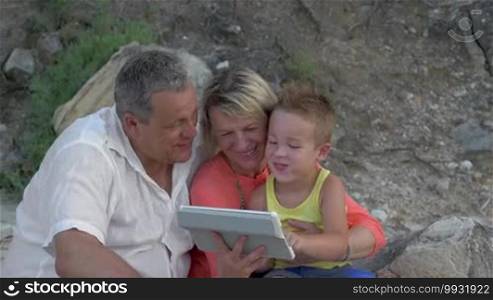 Grandmother, grandfather, and little grandson using a tablet computer during leisure time outdoors