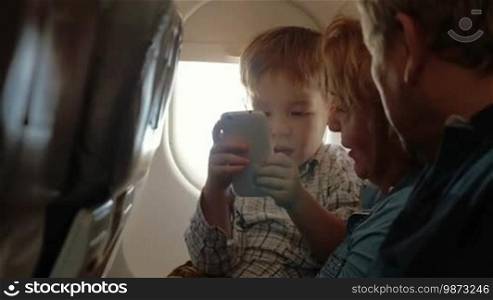 Grandparents talking to the grandson who is enjoying a smartphone while traveling by plane