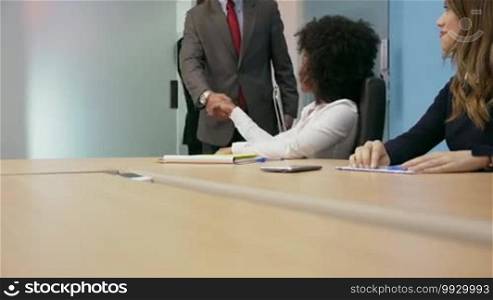 Group of business people meeting in corporate conference room, shaking hands and examining documents in team. Medium shot, copy space