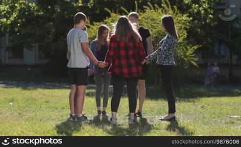 Group of Christian college students in a circle holding hands and praying for good exam results while standing on green grass on the university campus. Young teenage friends showing unity on the park lawn.