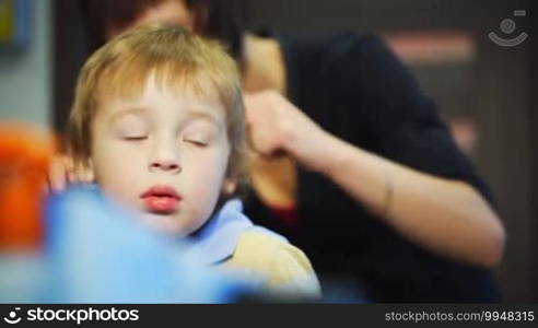 Hairdresser combing hair of the little boy before haircut. Focus on the lovely calm boy