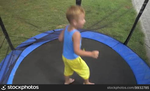 Handheld shot of a little boy jumping on outdoor tramp protected with net. Active leisure and fun in summer