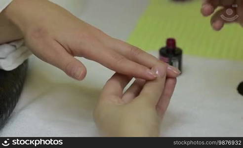 Hands of nail master painting female nails with red lacquer. Closeup finger nail care by manicure specialist in beauty salon. The beautician applying gel polish shellac on woman's fingernail. Healthcare beauty cosmetic spa procedure in salon.