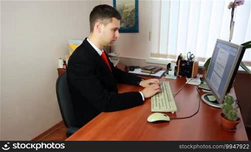 Hands!ome young man in suit with red tie, typing some documents at work