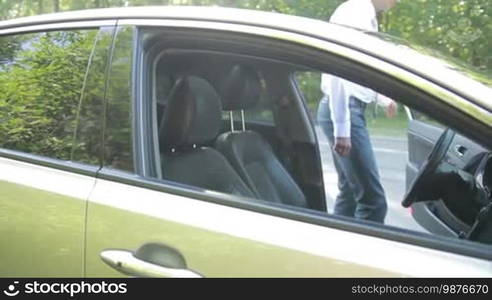 Handsome young businessman in stylish clothes fastening seat belt ready for driving. Side view. Confident man getting into car and fastening safety belt before going on business trip. Slow motion. Steadicam stabilized shot.