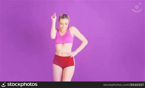 Happy beautiful woman in sports shorts with a bare midriff dancing on a purple background laughing and smiling at the camera with copyspace