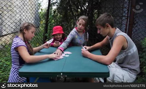 Happy children play playing cards, sitting at a table in the yard