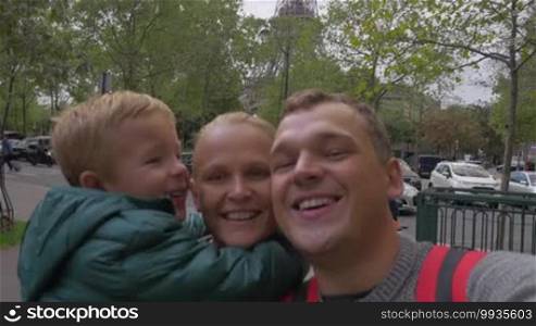 Happy family of mother, father, and little son making a selfie video against the Eiffel Tower. Visiting Paris, France