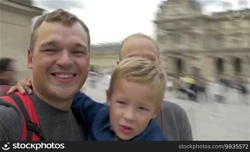 Happy father, mother, and child visiting Louvre in Paris. They are making a spinning selfie video and smiling