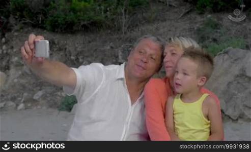 Happy grandmother, grandfather, and grandchild taking a selfie with a smartphone outdoors. Family shot as mementos