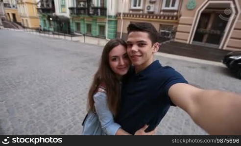 Happy hipster couple in love taking self portrait with smartphone while enjoying time together in city streets during travel on vacation. Attractive couple making selfie on smartphone outdoors.