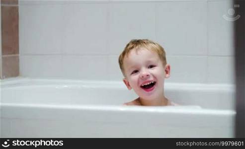 Happy laughing boy sitting in the bath