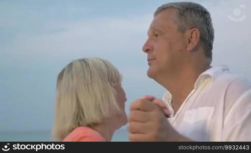 Happy mature couple is dancing outdoors, blue sky in the background.