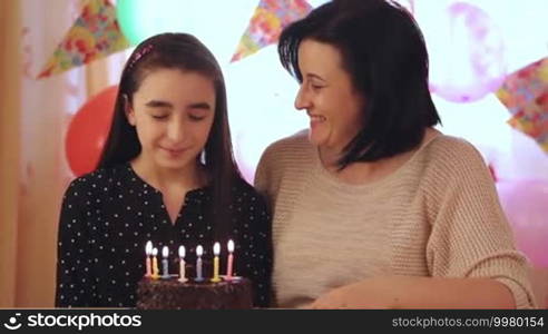 Happy mother and daughter blowing candles of birthday cake