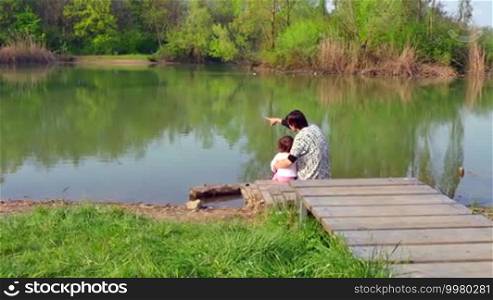 Happy people, family, lifestyle, leisure, nature, spring recreation, fun. Mother hugging daughter, mom and child, woman, baby, girl, sitting on wooden dock, looking at lake, natural landscape. 5of8