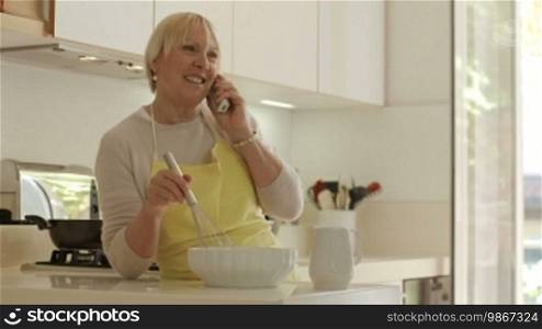 Happy senior women at home, cooking in the kitchen and talking on the phone