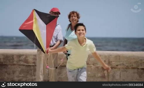 Happy tourists on holidays, during vacation journey. Hispanic people traveling in Havana, Cuba. Grandpa, grandma and grandson having fun near the sea. Family trip, boy running with kite, child playing