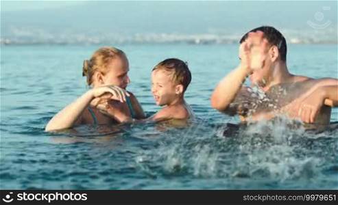 Happy young parents and little son fooling and splashing sea water. Family fun on summer vacation
