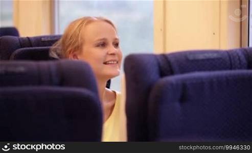 Happy young woman traveling by train and looking out the window.