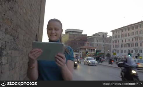 Happy young woman with tablet computer having video chat while walking along busy street in Rome, Italy