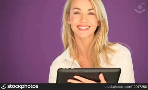Head and shoulders view of a happy attractive blonde student working on a tablet she is holding in her hand