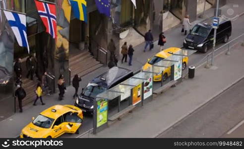 High angle shot of people coming out of main entrance of Tallink City Hotel. Flags fluttering above the entry, taxi cars parked nearby