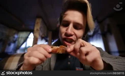 Hipster eating delicious roasted chicken wing at the restaurant. Low angle view closeup. Teenager enjoying the snack in a cafe while having lunch with friends.