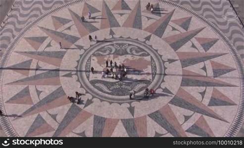 Historical square made of stone mosaic in Lisbon. Monument of the Discoverers. It depicts the world map and the most important exploratory journeys are marked. People are in the square.