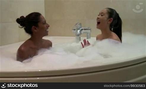 Homosexual couple, gay people, young lesbian women, same-sex marriage relationship between happy girls in the bathroom. Naked sexy lesbians smiling, laughing, talking in a Jacuzzi bathtub with soap bubbles