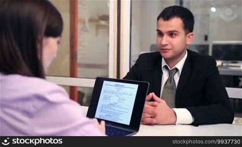 Human resource manager is hiring a new employee. Businesswoman sitting at the table with laptop and listening to a young businessman. Female recruiter asking questions to handsome man in business suit during job interview.