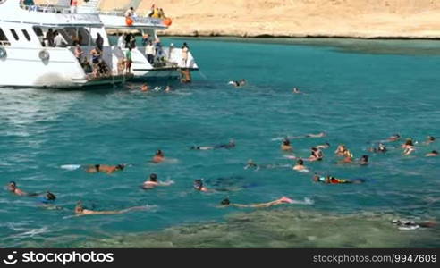 HURGHADA, EGYPT - FEBRUARY 1, 2014: Tilt shot of a group of people swimming in coastal water near the yacht